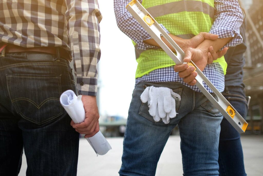 3 construction monitors looking at construction site with level, gloves and rolled up paper