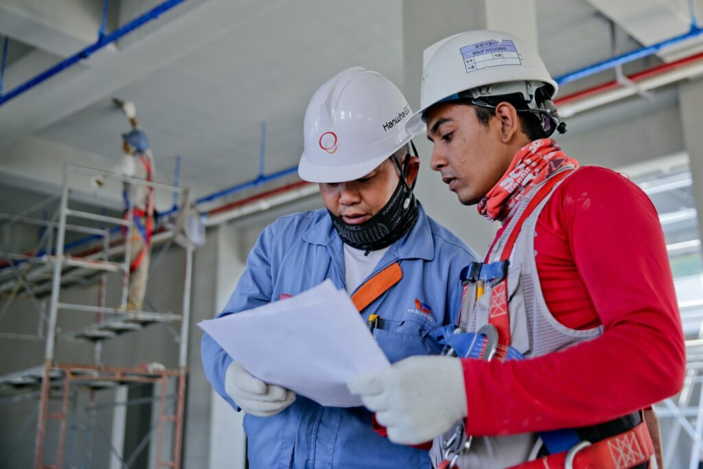 Two construction workers with hard hats looking at a monitoring report prepared by Saltus at an active construction site.