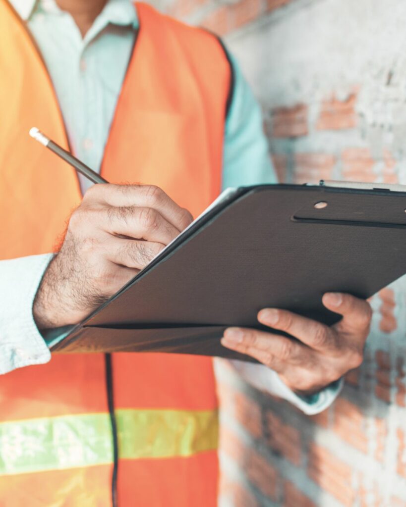 Man wearing an orange construction vest holding a clipboard.