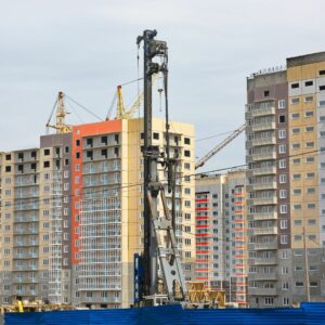 A pile driver on a construction site surrounded by several high-rise buildings.