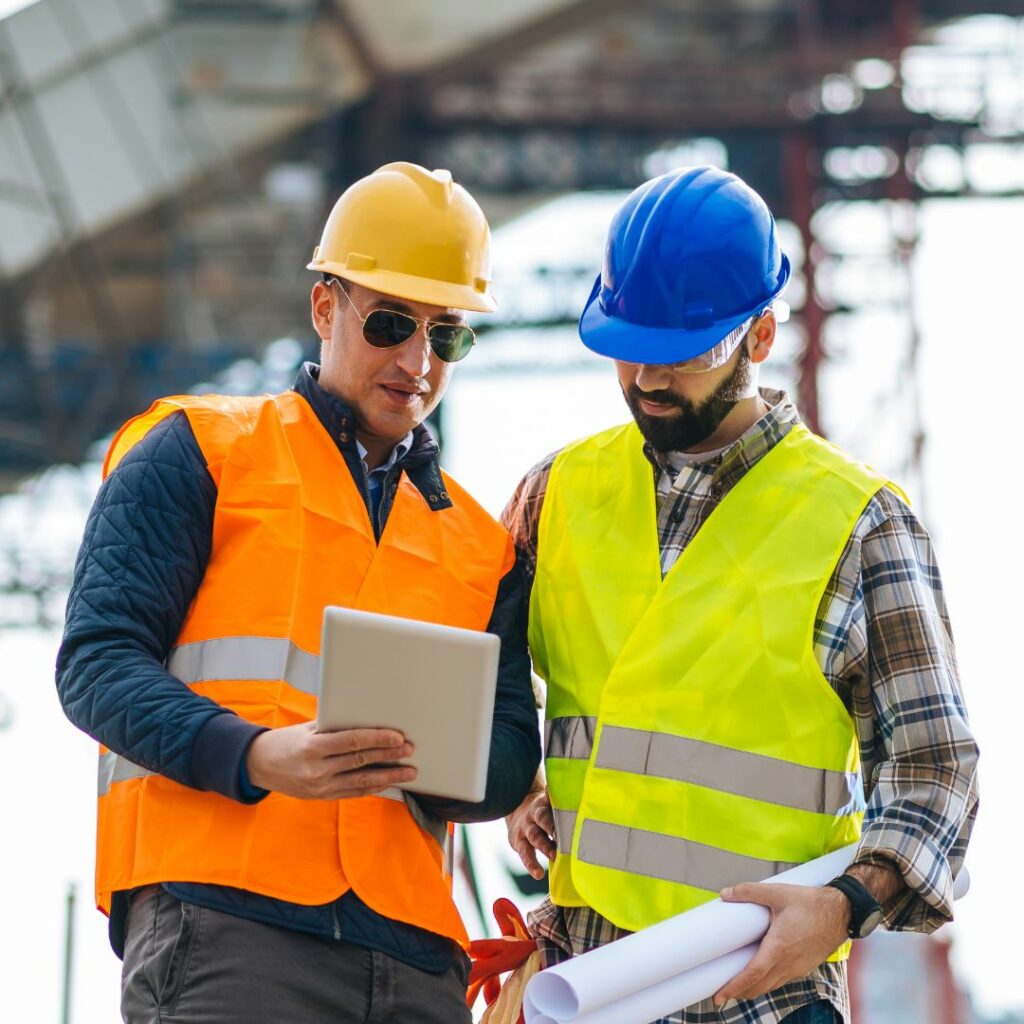 Two construction workers at a building site reviewing a Community Air Monitoring Plan on a tablet.