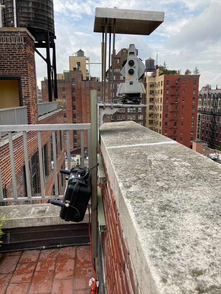 An Automated Total Station mounted on a bracket on top of a roof to monitor any potential movements in a neighboring property.