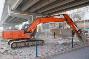 An excavator being used on a construction site beneath a highway overpass.