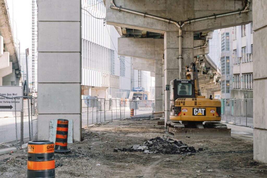 A piece of equipment on an active construction site beneath a commuter train overpass in a city.