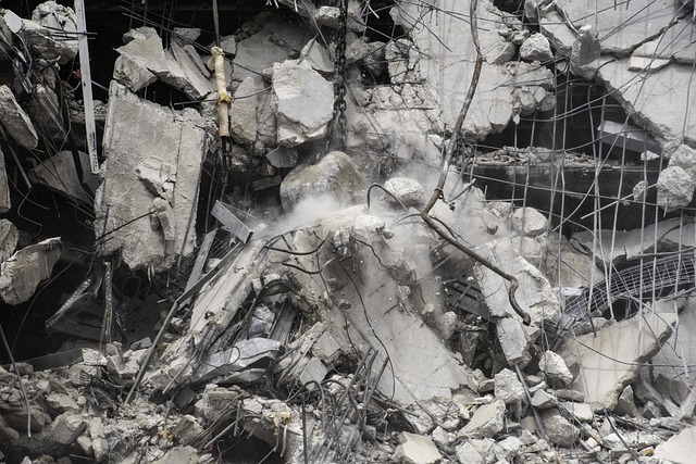 Demolition site with crumbling concrete slabs, exposed rebar, and airborne dust rising from collapsed building debris.